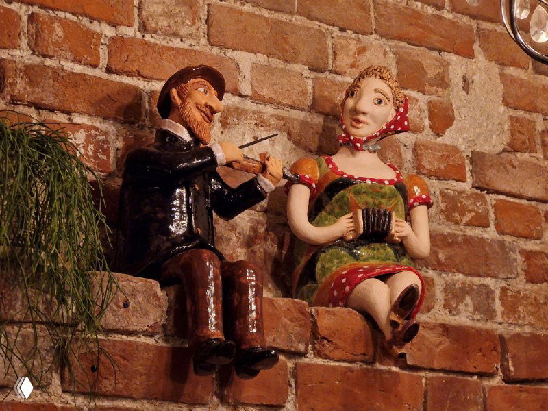 Керамические фигурки музыканта и девушки на кирпичной стене внутри ресторана; интерьерная деталь, подчёркивающая атмосферу заведения.