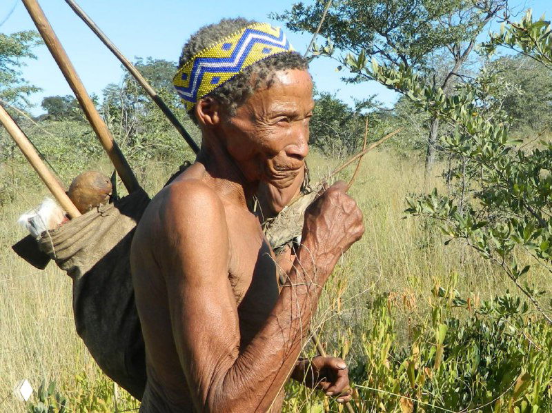Портрет пожилого члена племени сан в Намибии в ярком орнаментированном наголовье, лицо и руки с заметными морщинами и жизненным опытом.