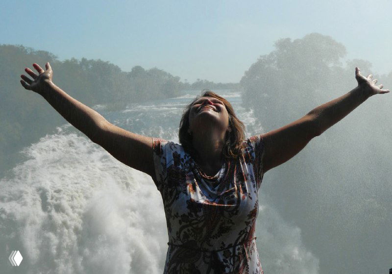 Человек с распростёртыми руками на фоне брызг и тумана водопада — ощущение контакта с природной стихией и радости от водной пыли.