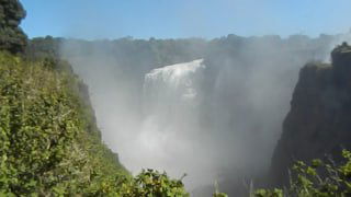 Сильный туман и водяная пыль скрывают часть каскадов Виктории, вид издалека на реку и удаляющиеся уступы водопада в дымке.