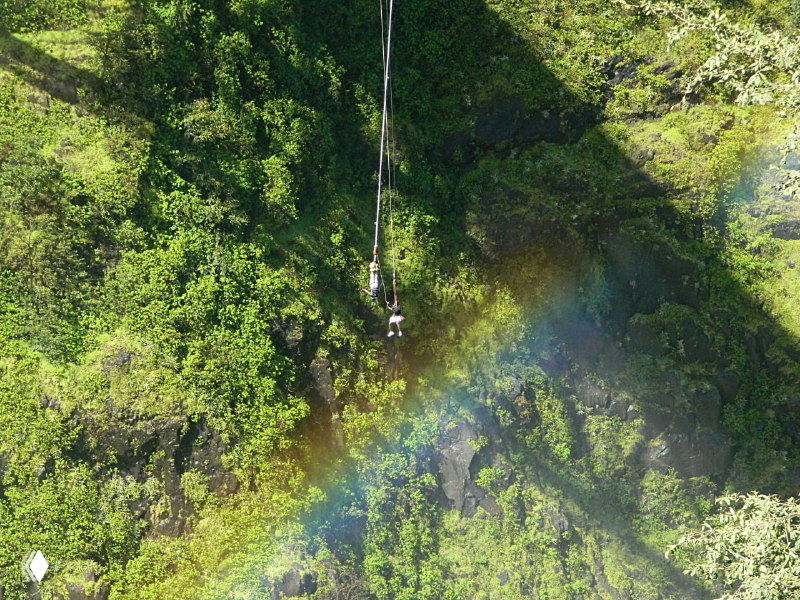 Человек на зиплайне над ущельем Замбези: тросовая переправа высоко над рекой, внизу видны склоны и зелень каньона.