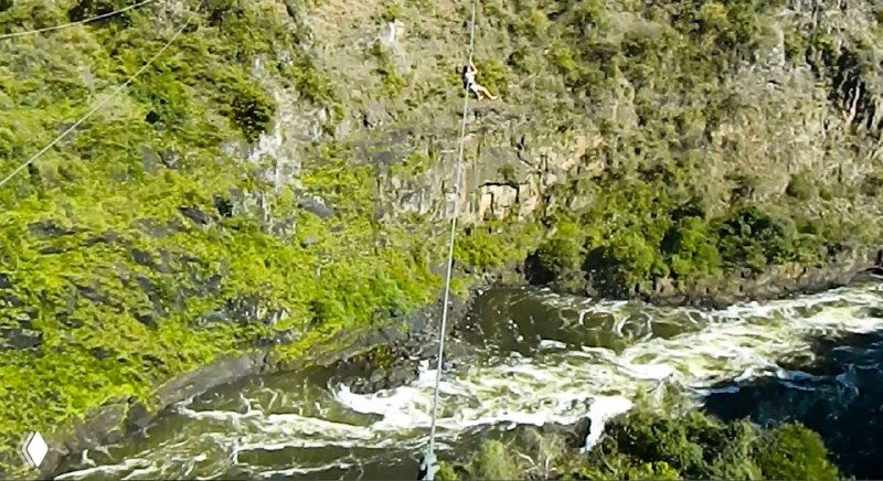 Трос зиплайна, висящий над стремительной поверхностью воды Замбези, кадр показывает переправу и пенящиеся струи под ней.