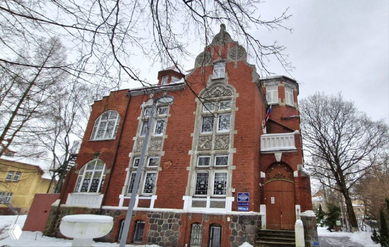 Массивное кирпичное здание в стиле модерн с высоким фронтоном и большими декоративными окнами на фоне зимнего неба.