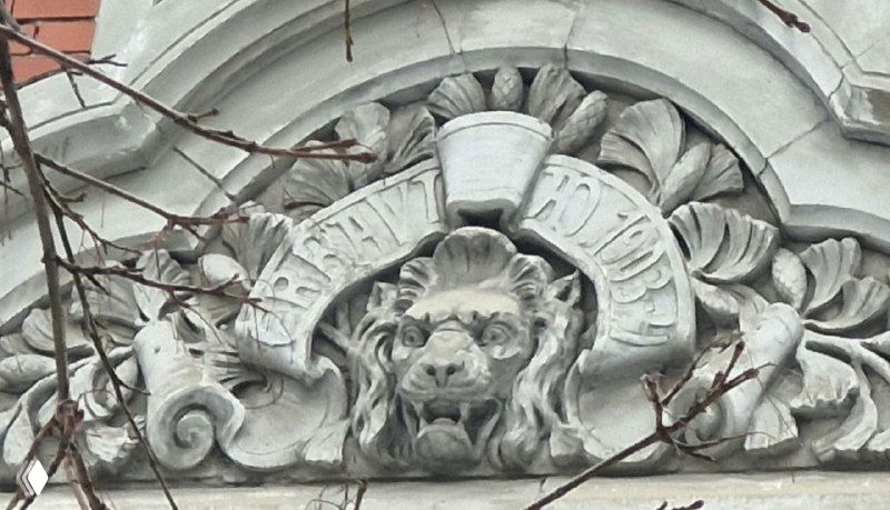 Архитектурный декор: каменная маскарон-голова льва и растительный орнамент над входом старинного дома, снято крупным планом.
