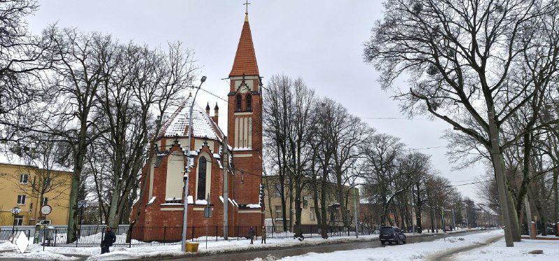 Неоготическая кирпичная церковная постройка с остроконечной башней и арочными окнами вдоль улицы, зимой без людей.