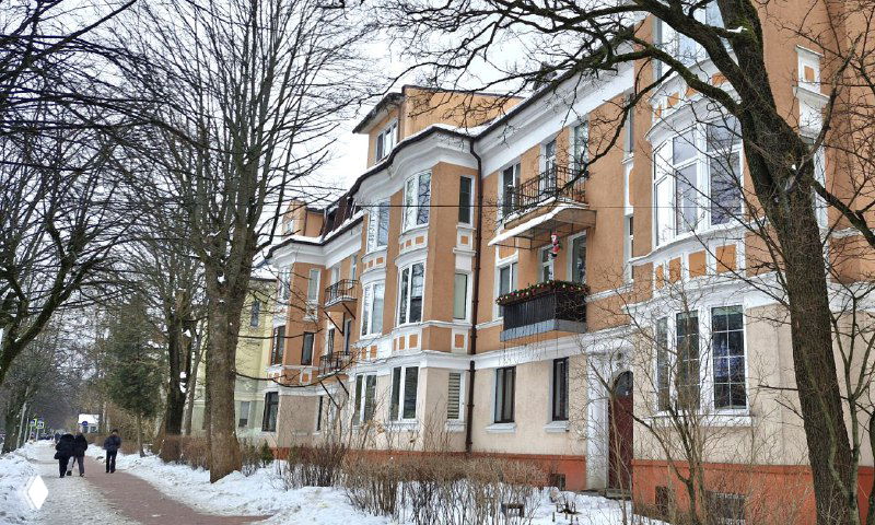 Ряд жилых зданий в стиле модерн вдоль улицы: светлые стены, балконы, декоративные наличники и заснеженные тротуары.