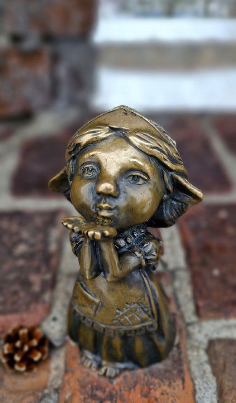 Бронзовая фигурка малышки-хомлины, посылающей воздушные поцелуи, крупный портретный план на фоне городской поверхности.