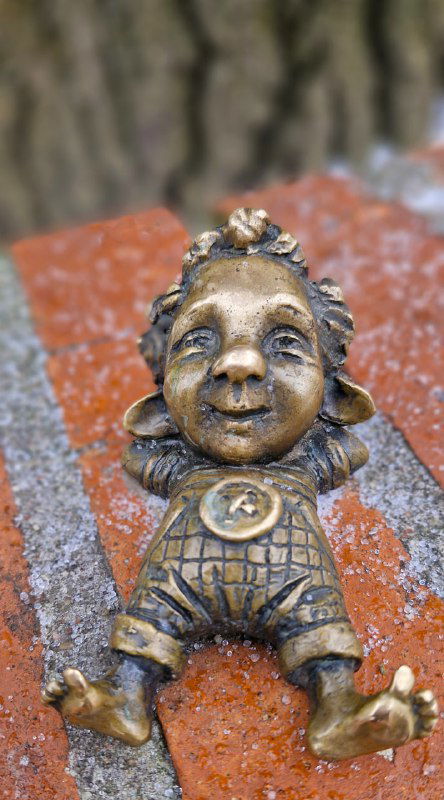 Небольшая бронзовая фигурка ребёнка на кирпичной поверхности: портретный план, видны черты лица и элементы одежды на скульптуре.