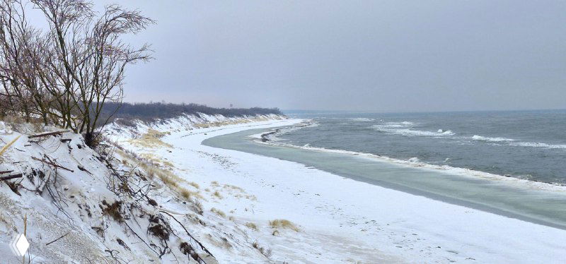 Долгая извилистая береговая линия Куршской косы с заснеженными склонами дюн и тонкой полоской моря, вида с обзорной точки.