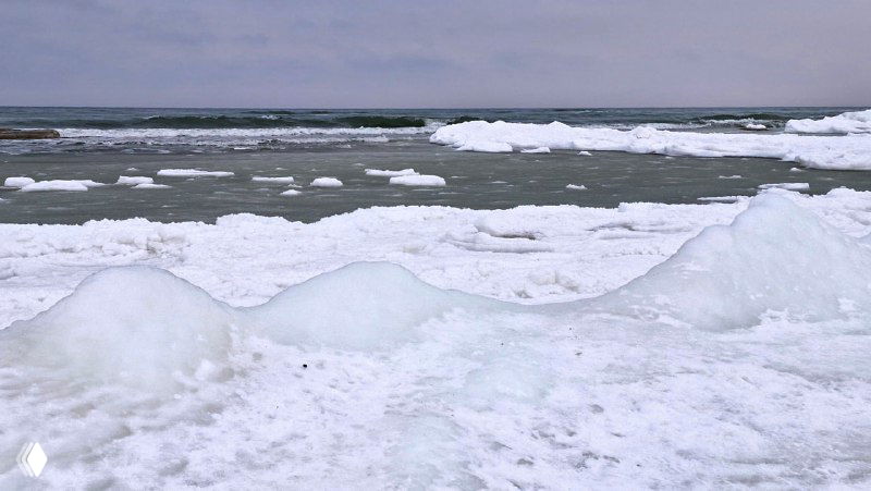 Замерзшие волны и льдины у берега Балтийского моря: снежные накатки и ломкие пласты льда среди прибрежной воды.