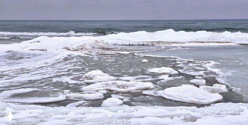 Побережье с плавающими кусками льда и перемешанным снегом, узоры льда и воды на мелководье в зимний пасмурный день.