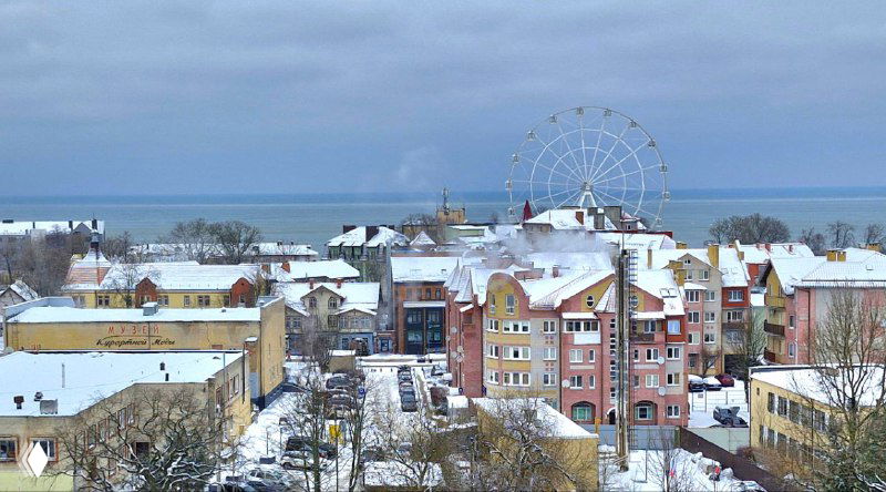 Вид на набережную с колесом обозрения и разноцветными домами на фоне моря; зимний городской пейзаж Зеленоградска как туристическая сцена у Балтики.