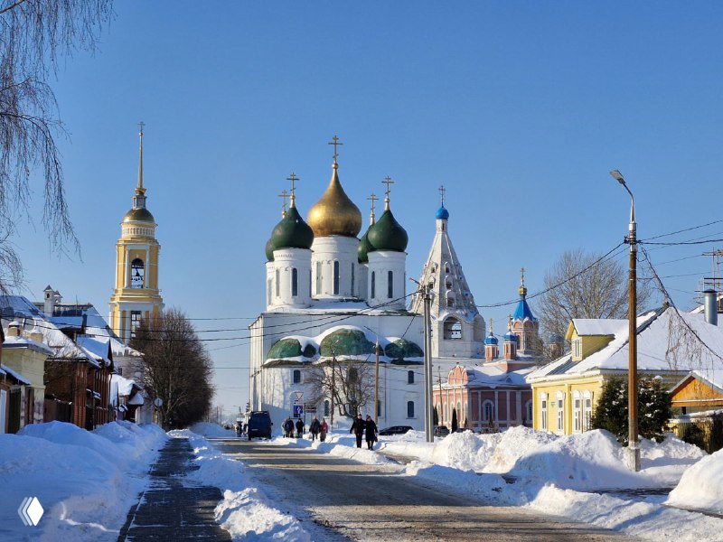 Улица, ведущая к белому собору с зелёными и золотыми куполами в Коломне, заснеженные дома по сторонам.