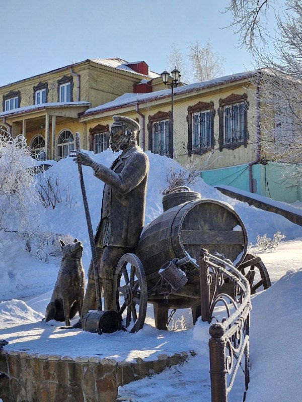 Скульптура Водовоза с бочкой и собакой на заснеженной площади Коломны, рядом видна шкала паводковых вод.