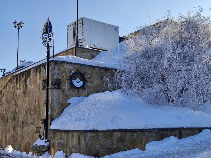 Каменная стена и заснеженные деревья у набережной Коломны, весенне-зимняя растительность в инее.
