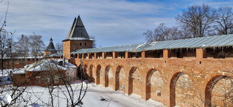 Длинная секция крепостной стены и аркады Зарайского кремля в снегу, вид вдоль оборонительного пояса и ворот.