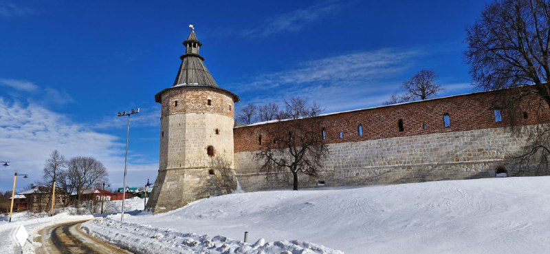 Круглая водонапорная башня и часть кремлёвской стены на заснежённом склоне в ясную погоду, доминирует архитектурный силуэт.