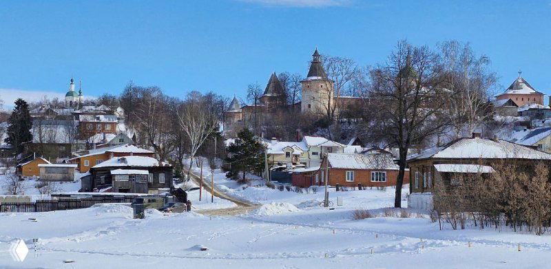 Панорамный городской пейзаж Зарайска: деревянные и кирпичные дома, белый снег и церковные силуэты на горизонте.