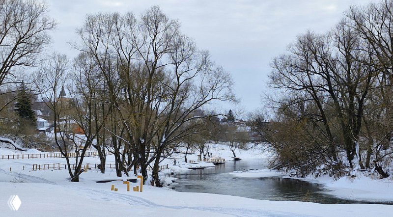 Река Осетр зимой: части берега покрыты снегом, спокойная вода и голые деревья вдоль новой набережной с помостами.