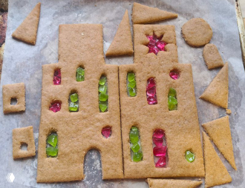 Заготовки из теста с вставленными кусочками цветных леденцов в отверстиях — будущие витражные окошки пряничного домика перед выпечкой.