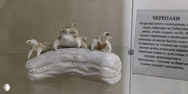 Белые резные черепахи и другие маленькие скульптуры из кости, расположенные в стеклянной витрине с подписью о материале и технике изготовления в музее Тобольска.