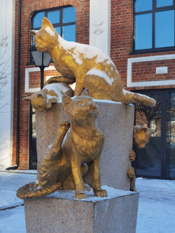 Бронзовые и чугунные фигуры котов на постаменте в Тюмени, разные позы скульптур и снежные отложения на поверхности памятника.