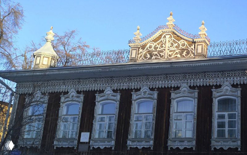 Фасад купеческого особняка в Тюмени с тонкой ажурной резьбой по карнизу и декоративными элементами на крыше и наличниках окон.