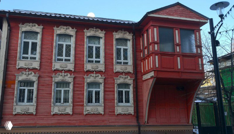 Красный деревянный дом с эркером и резными наличниками вокруг окон: традиционные формы и цветовое выделение элементов архитектуры.