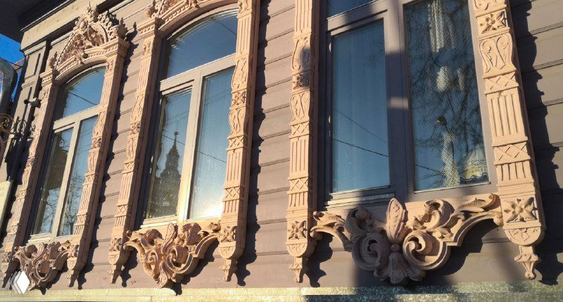 Светлый фасад с высокими окнами и лепниной: подоконные доски украшены объемной резьбой в виде цветов и виноградных гроздей.