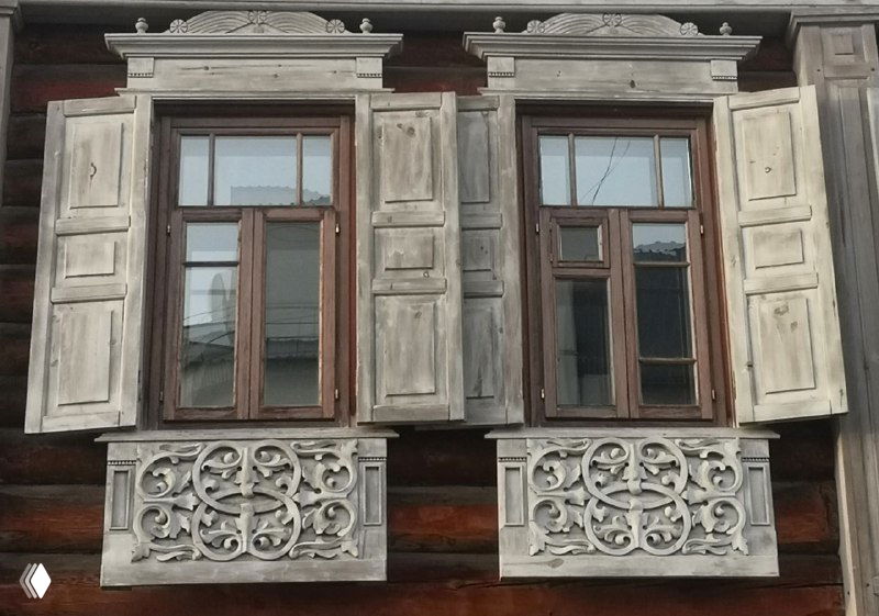 Окна с простыми ставнями и декоративными круглыми элементами внизу — пример более сдержанной тюменской деревянной резьбы на жилом доме.