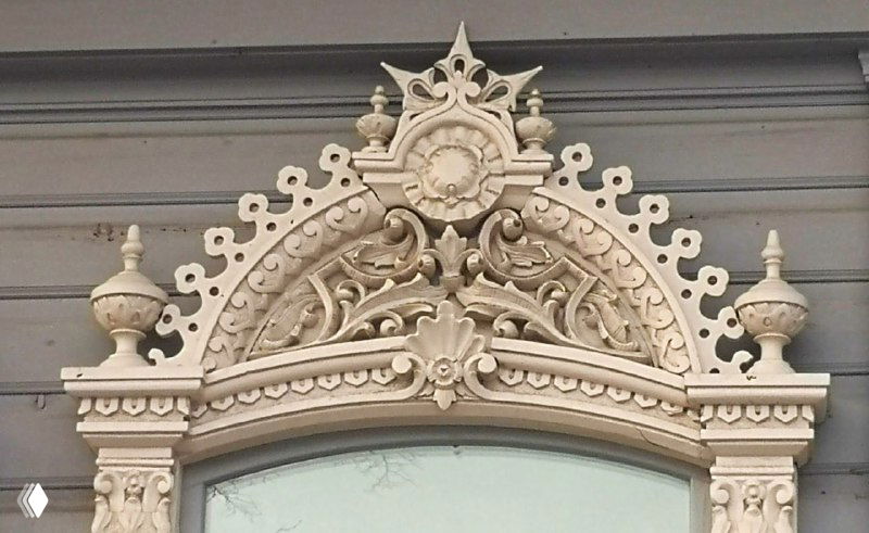 Изящный резной орнамент над окном в виде венчика и короны украшает фасад, демонстрируя мастерство тюменских резчиков по дереву.