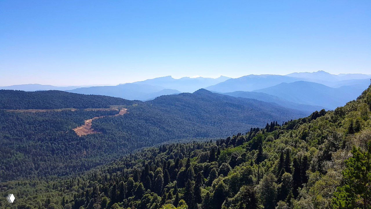 Широкий вид с гребня на мористую долину и горные отроги Лагонаки: слои лесистых склонов уходят в туманную глубину, подчёркивая масштаб местности.