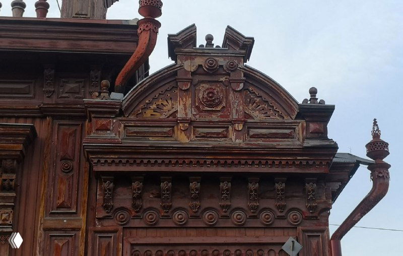 Сложная деревянная резьба на угловой части особняка: ампирные и растительные символы в плотной композиции, характерной для купеческих домов.