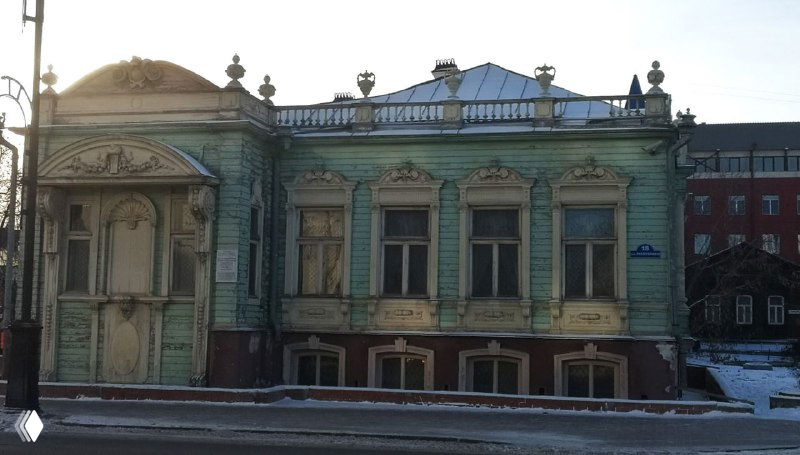 Павильонный фасад светлого деревянного дома в историческом центре Тюмени, вид в зимнее время с улицы и заснеженной крышей.