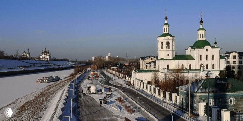 Панорамный вид на набережную и Троицкий монастырь с зелёными куполами и белыми стенами, церковная архитектура на фоне реки.
