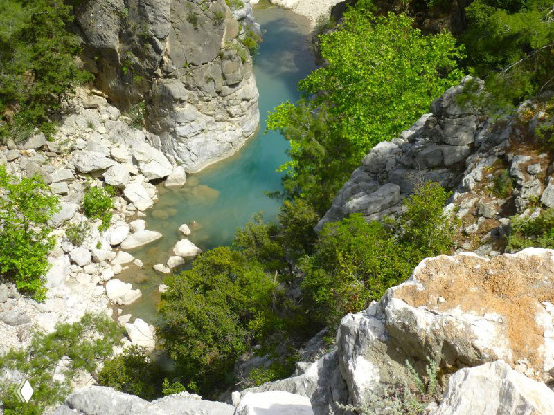 Долина и уступы каньона с бирюзовыми лужами воды между скалами; резкие скалы по обеим сторонам и зелень растительности.