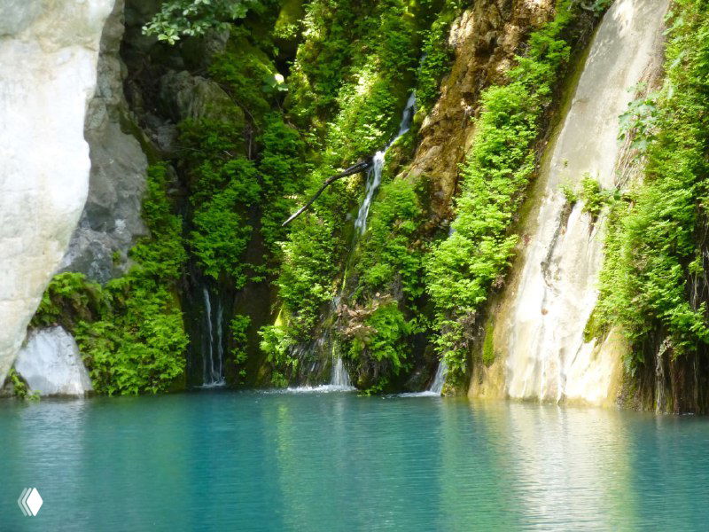 Голубая лагуна и маленькие каскадные водопады внутри каньона; гладкая поверхность воды, окружённая скалами и зеленью.