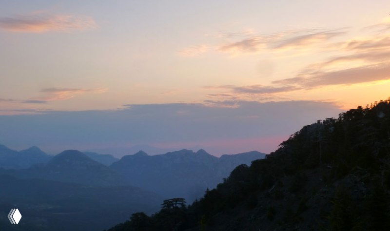 Закатный горизонт над горными вершинами: пурпурно-оранжевые оттенки неба и силуэты хребтов вечером после подъема.