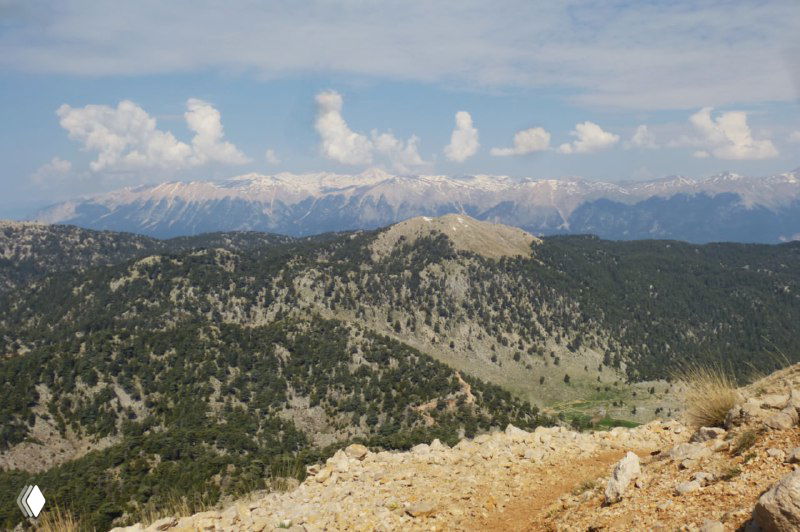 Панорамный вид на лесистые склоны и дальние горные хребты Ликийской тропы под голубым небом, показывающий направление дальнейшего движения.
