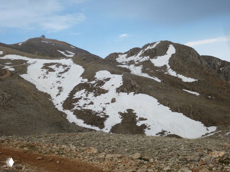 Каменистые склоны с остатками снежных полей на подходе к вершине Тахталы — крупный план горных гряд и снежных лоскутов в верхней зоне.