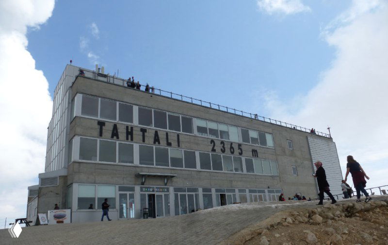 Здание на вершине Тахталы с посетителями на крыше и входом в сооружение — станция фуникулёра и кафе, видна активность туристов у сооружения.