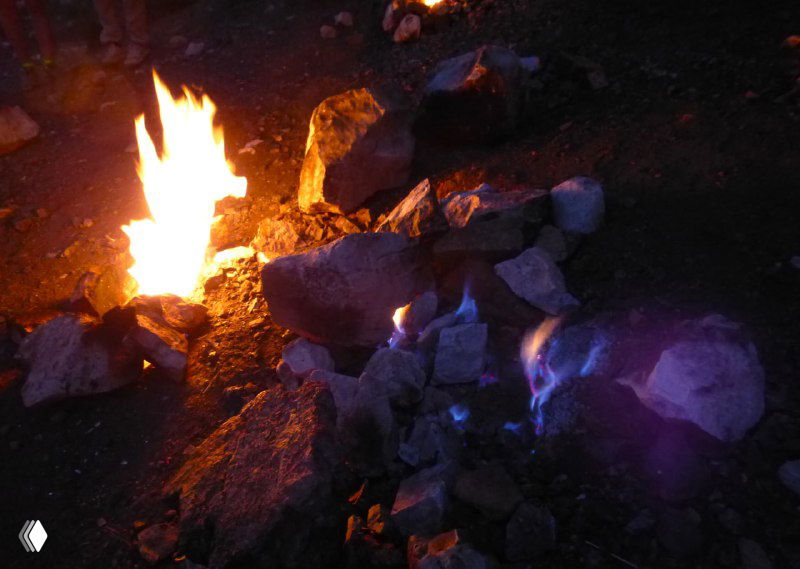 Несколько небольших огоньков, вырывающихся из каменных расщелин на тёмном грунте — съемка ночью, видны яркие пятна пламени.