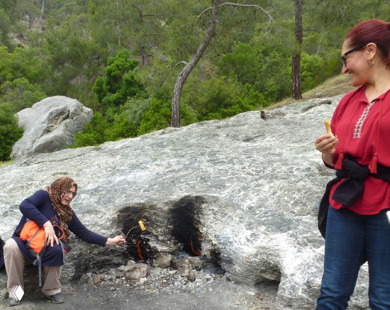 Местные люди у расщелины с горящим пламенем на скале, рядом туристы и каменные образования — социальный контекст посещения Янарташа.
