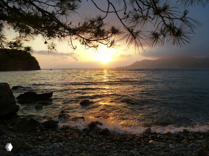 Закат над морем: солнце садится за горизонт, отражения в воде и тёплые оттенки неба над береговой линией Чиралы.