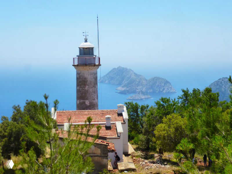 Маяк на мысе Гелидония на фоне моря и островов, белое здание и башня-ориентир для моряков и туристов на Ликийской тропе.