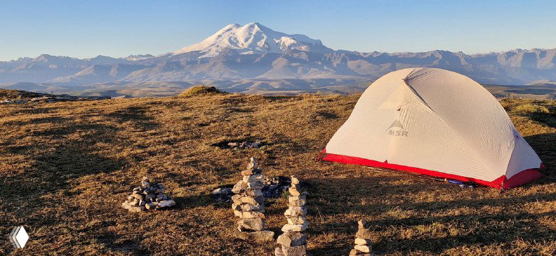 Белая палатка MSR Hubba Hubba NX на плато Бермамыт с панорамным видом на заснеженную вершину Эльбруса и широкий горный горизонт.