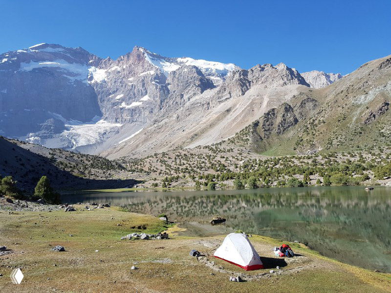Палатка MSR у высокогорного озера во Фанских горах: отражение снежных вершин в зеркальной воде и просторная прибрежная стоянка.