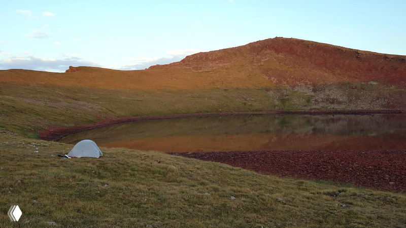 Палатка MSR в рассветных тонах на холме рядом с небольшим озерцом — широкая панорама и отдалённые горы на фоне неба.