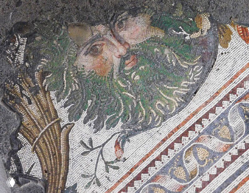 Декоративный круглый медальон с лиственным и человеческим лицом на мозаике — орнаментальный элемент пола Большого дворца, сохранённый в музее Араста.
