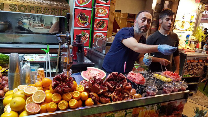 Уличная прилавочная лавка с фруктами, гранатами и ингредиентами для стрит‑фуда на Истикляль; продавцы готовят свежие закуски для туристов.